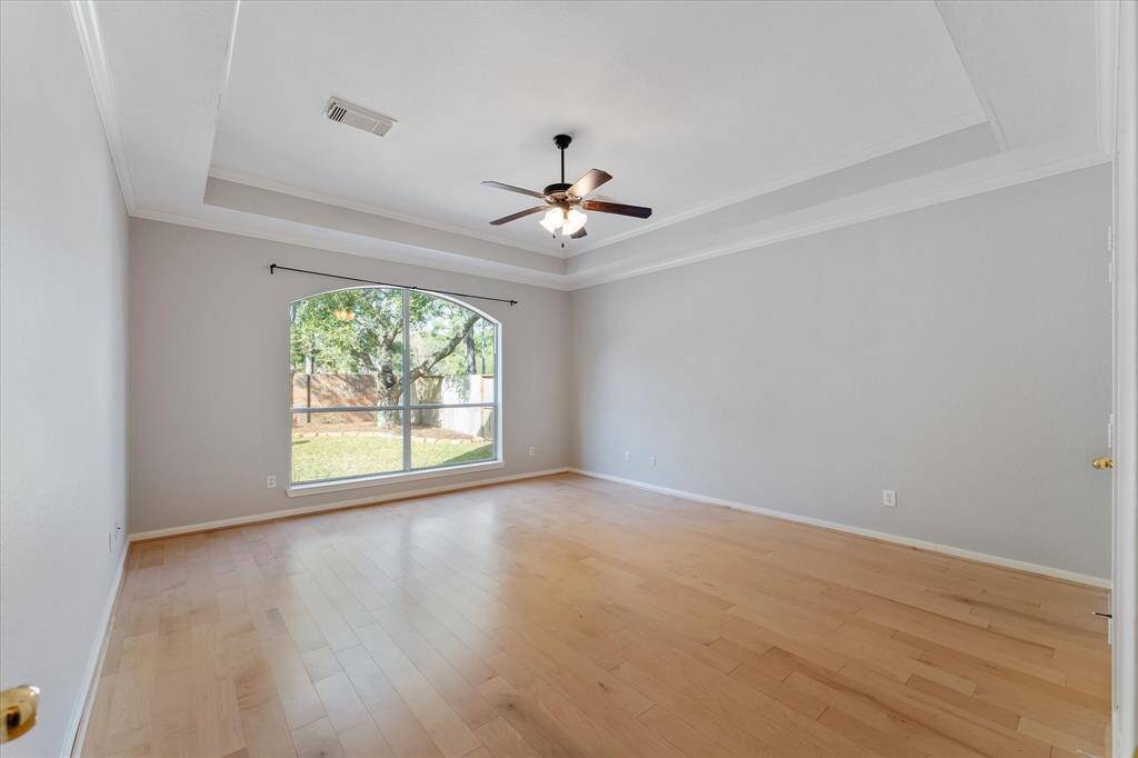 Large primary bedroom featuring tray ceiling and wood floors.