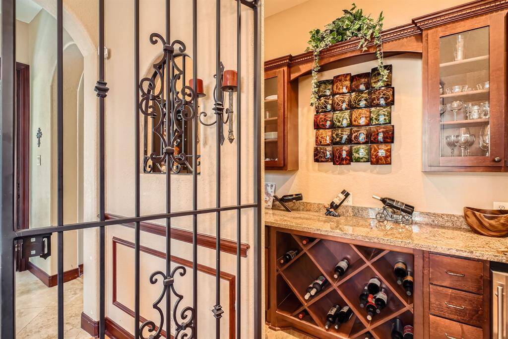 This photo depicts the entrance to the grotto bar area with wooden cabinetry, granite countertops, and a wine rack. Decorative metalwork and wall art add elegance, while glass-front cabinets display glassware. A metal gate provides a unique touch.