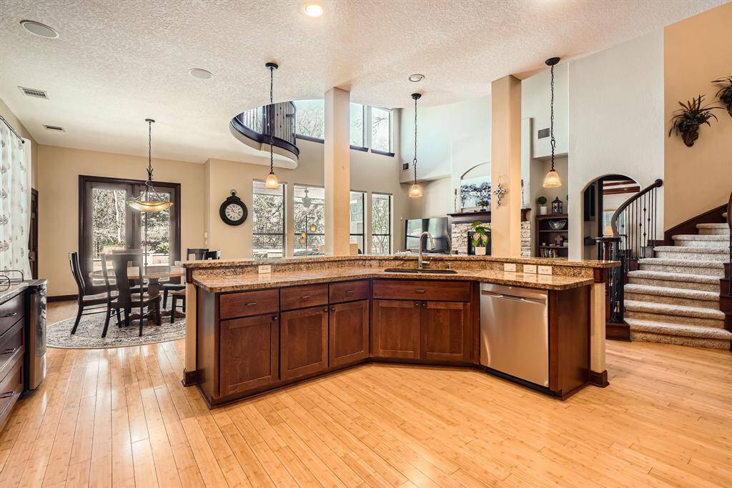 This spacious and elegant kitchen features a large island with granite countertops, modern stainless steel appliances, and warm wood cabinetry. It opens to a bright dining area with large windows and a beautiful spiral staircase, creating a perfect blend of style and functionality.