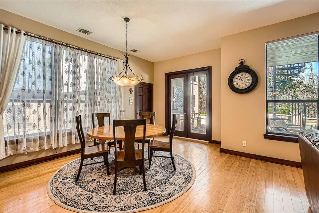 Natural light pours in through large windows of this dining area. French doors open to an outdoor view. The space boasts warm wood flooring throughout.