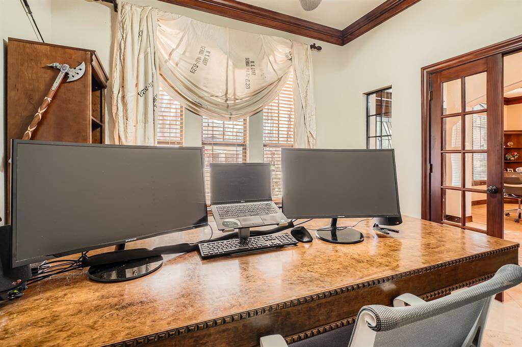 This home office features a spacious desk and a wood-framed window providing natural light. It has elegant wood trim and French doors leading to another room, creating a professional and inviting workspace.