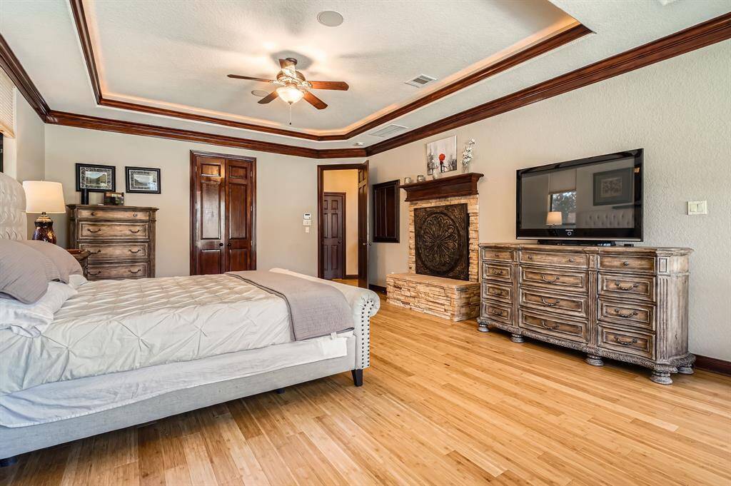 Spacious and well-lit bedroom featuring hardwood floors, a tray ceiling with recessed lighting, and large windows providing a view of the outdoors. The room is elegantly furnished creating a warm and inviting atmosphere.