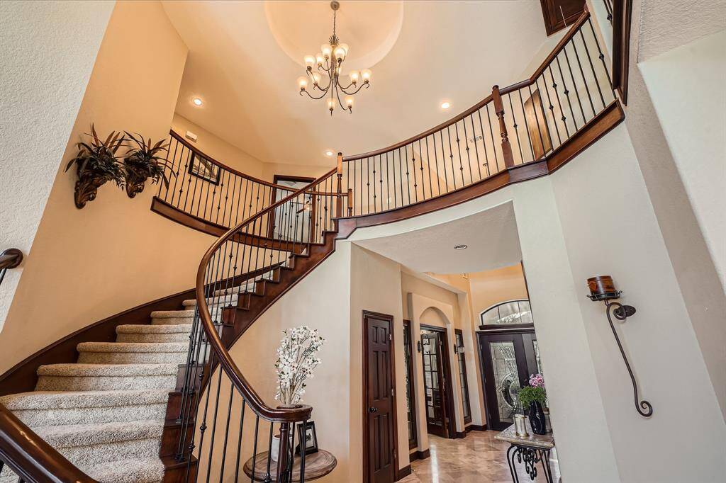 This photo showcases a grand, elegant foyer with a sweeping curved staircase featuring dark wood railings and iron balusters. The high ceiling is adorned with a centered chandelier for a dramatic effect.