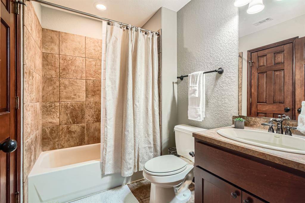 This bathroom features a warm, inviting design with a tiled shower-bath combo, a sleek vanity with a modern faucet, and a wooden door. The neutral tones and clean lines create a cozy and functional space.