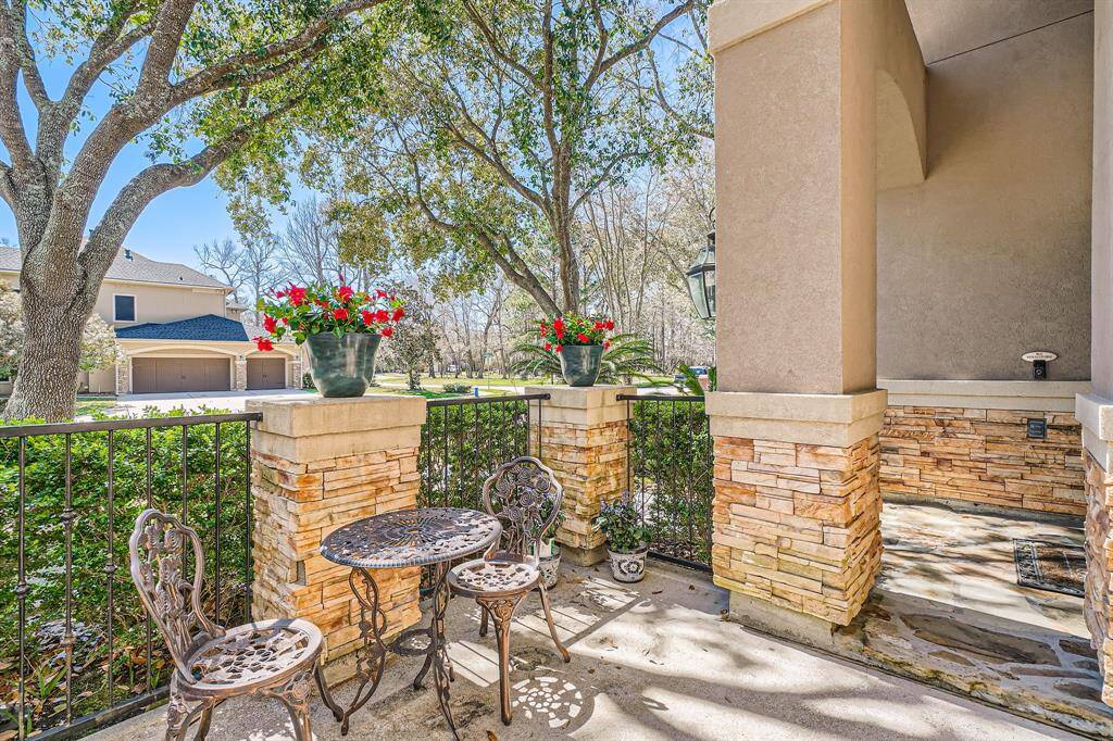 Charming outdoor patio area featuring a small wrought iron table and chairs, surrounded by a low stone and wrought iron fence. The space offers shade from mature trees. A peaceful spot for relaxation while overlooking the park.