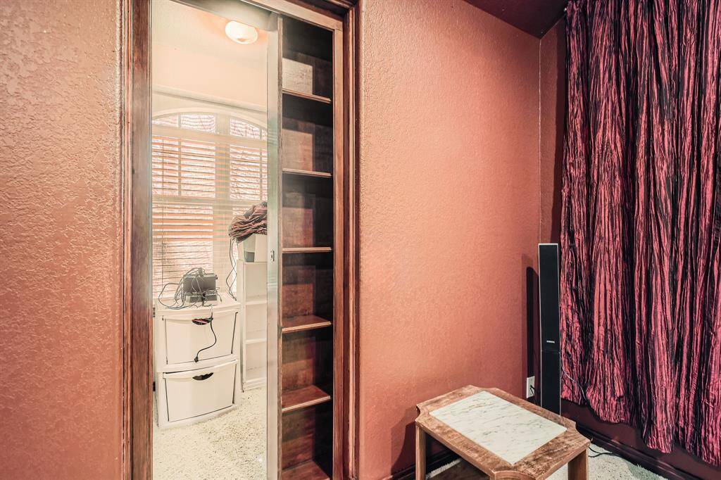 This photo shows a built in book case when opened revealing a secret feature for storage and a glimpse of a window with blinds.