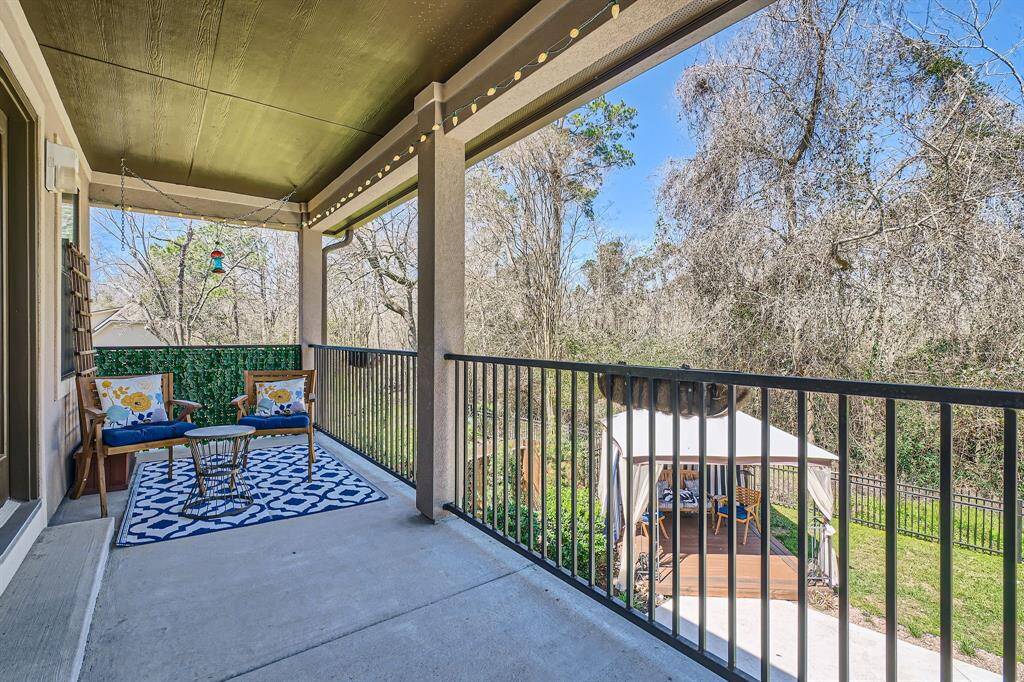 Charming covered veranda from the bedroom overlooking a lush backyard with a gazebo. Features cozy seating, decorative lighting, and a serene view of trees, perfect for relaxation and entertaining.