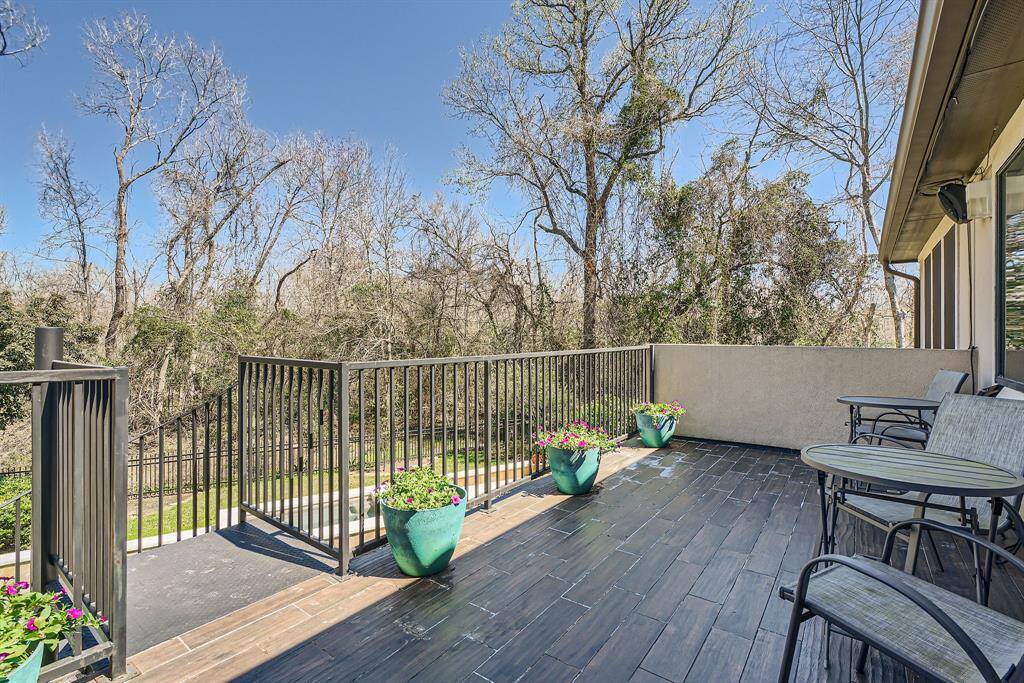 This photo showcases a spacious outdoor patio with modern railing, surrounded by trees for a natural view. The patio features stylish tile flooring and seating offering a peaceful spot for relaxing or entertaining.