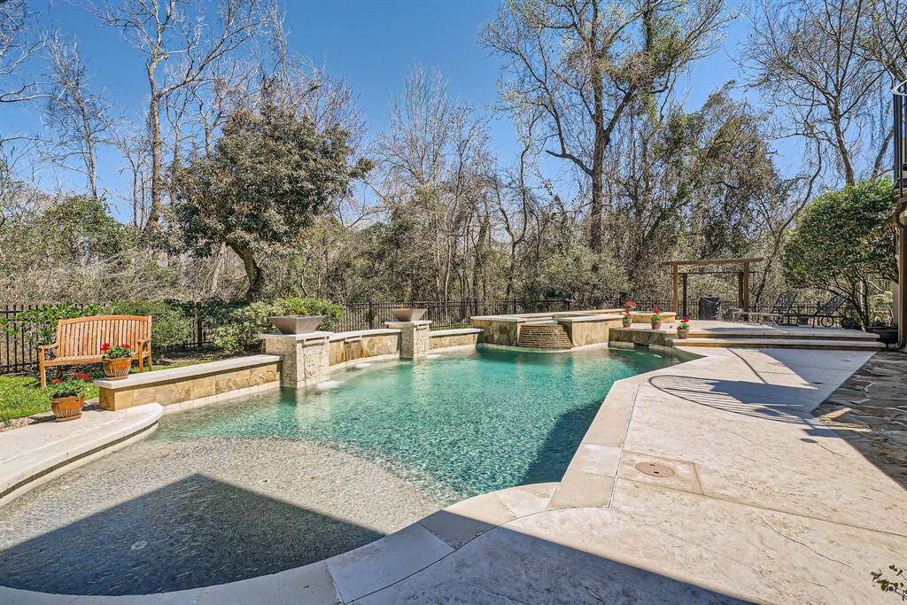 This backyard features a spacious pool with a stone water feature, surrounded by a landscaped area with mature trees for privacy and perfect for relaxation and entertaining.