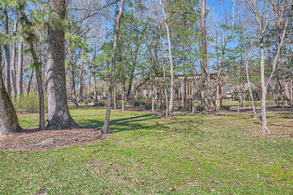 This photo showcases a serene wooded area park with a lush green lawn and a charming wooden pergola, offering a peaceful outdoor space ideal for relaxation and nature enjoyment all within a few steps from the house.