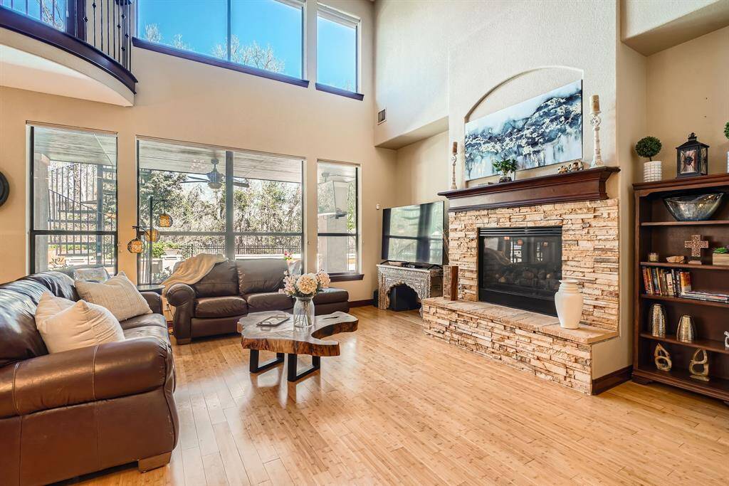 This spacious living room features high ceilings and large windows that provide plenty of natural light. It includes cozy seating and a stylish stone fireplace creating a warm and inviting atmosphere.