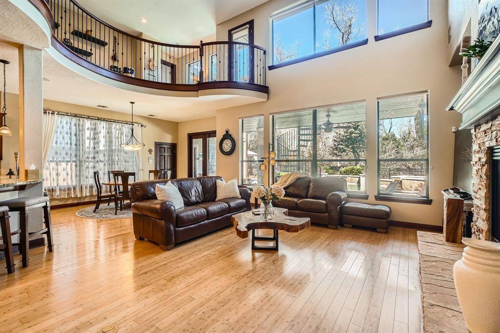 This spacious living room features high ceilings and large windows, allowing plenty of natural light. It includes a cozy stone fireplace, elegant wood flooring, and an open loft area above. The room is stylish and modern.