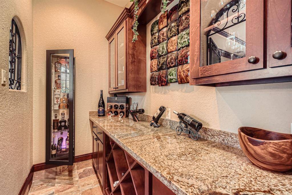 This photo showcases a stylish grotto area featuring granite countertops, wooden cabinets with glass fronts, and a sleek, illuminated liquor display cabinet. The space is accented with a decorative wine rack and artistic wall decor, creating a sophisticated and inviting atmosphere for entertaining.