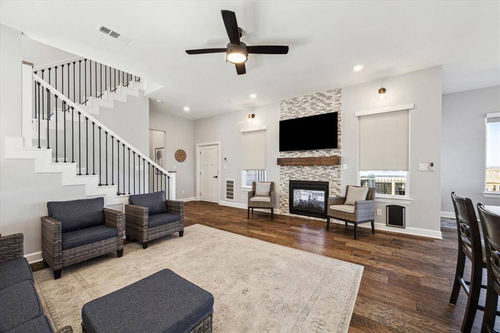 THE SPACIOUS DEN FEATURES A DOUBLE-SIDED FIREPLACE WITH STACKED STONE SURROUND, WOOD MANTLE, WALL-MOUNTED TV AND REMOTE WINDOW SHADES.