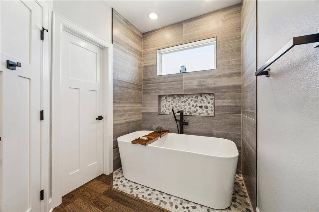 THE FREESTANDING TUB FEATURES FLOOR TO CEILING TILE SURROUND AND TRANSOM WIDOW FOR NATURAL LIGHT.