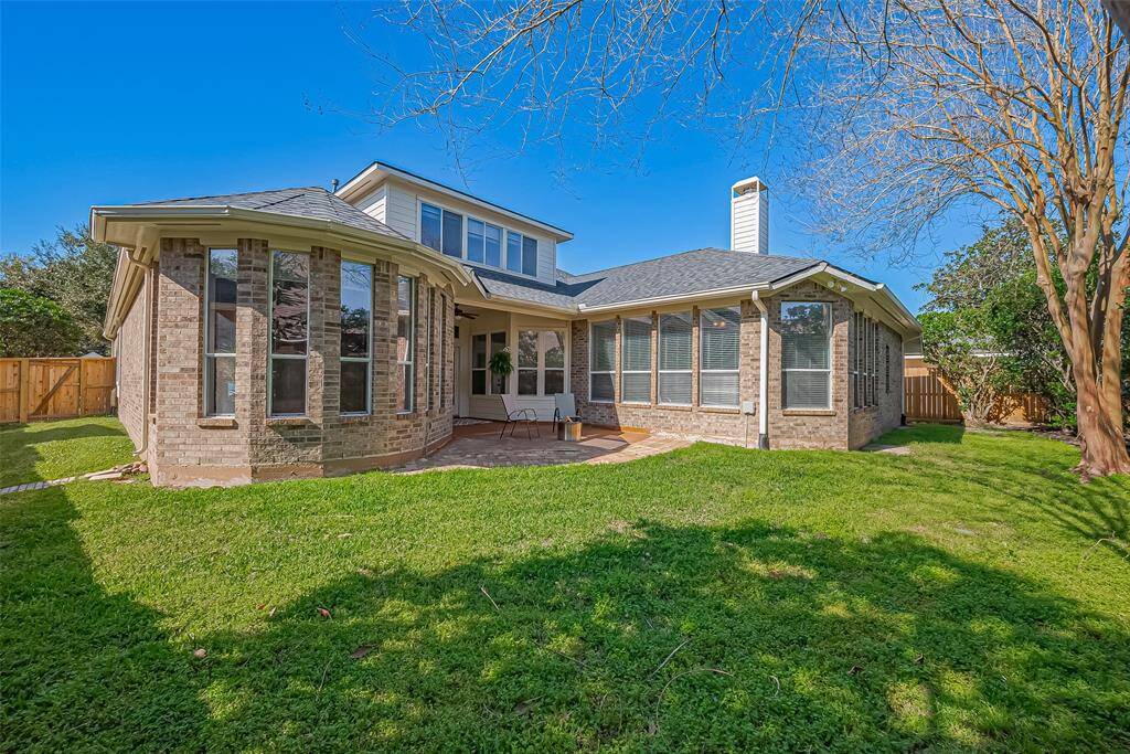 This home features a charming brick exterior with large windows, a spacious backyard, and a cozy patio area, ideal for outdoor relaxation.