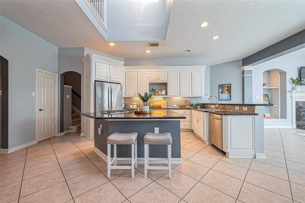 This kitchen features modern stainless steel appliances, white cabinetry, and a large central island with seating.