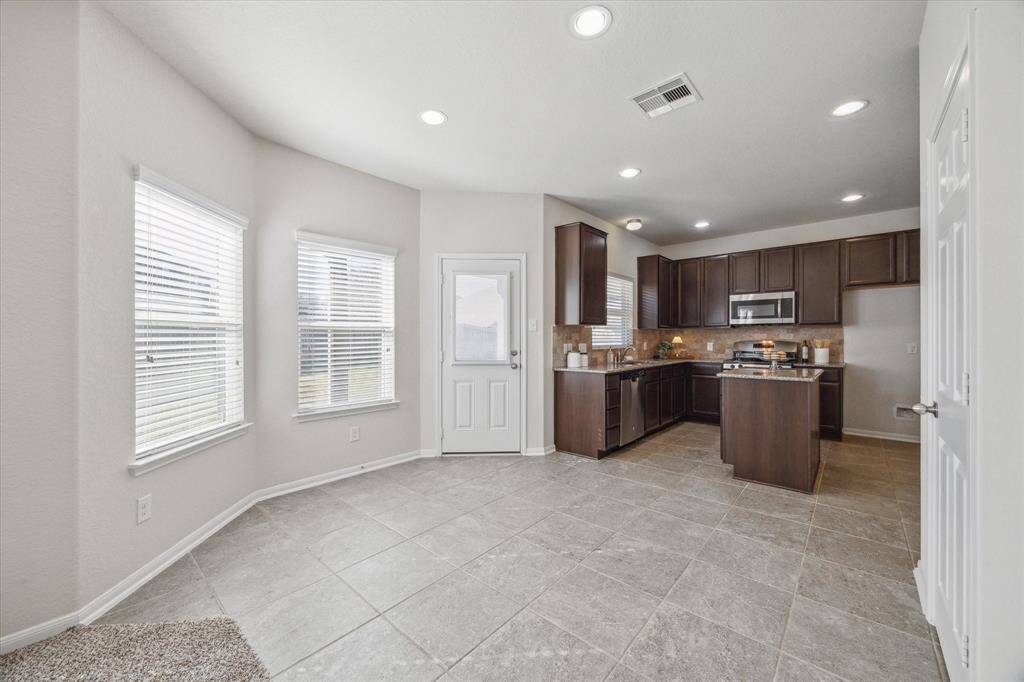 This spacious breakfast nook and view of the kitchen is awash in natural light. The back door steps out onto a covered patio.