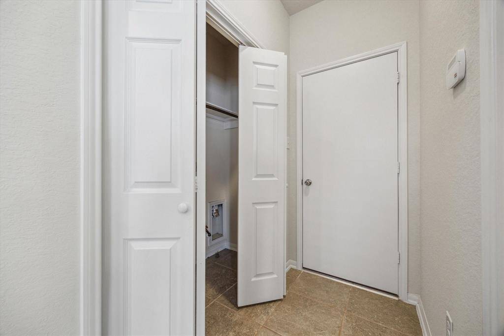 Located just off the kitchen, across from the half-bath, these convenient bifold doors keep laundry tucked away neatly. The door beyond leads to the two-car garage.
