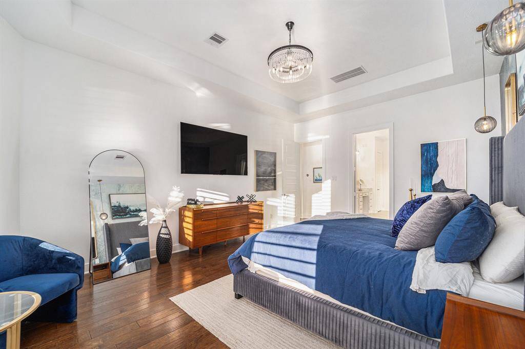 Oversized master bedroom featuring custom lighting, a unique wallpaper accent wall, plantation shutters, and elegant hardwood floors.