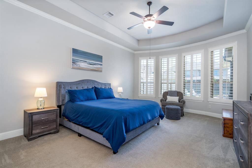 Welcome to your serene primary suite! A wall of windows with plantation shutters sheds light into a gorgeous tray ceiling adorned with crown molding!