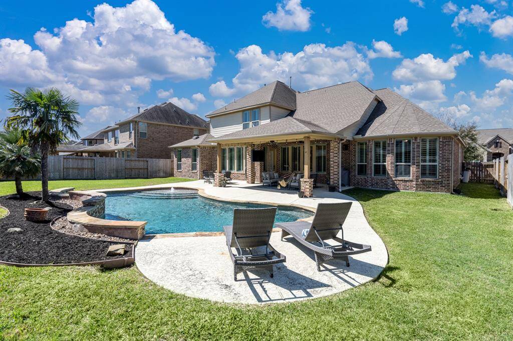 This view of the back yard highlights the large pool with extensive decking, huge covered patio, and abundant green space!