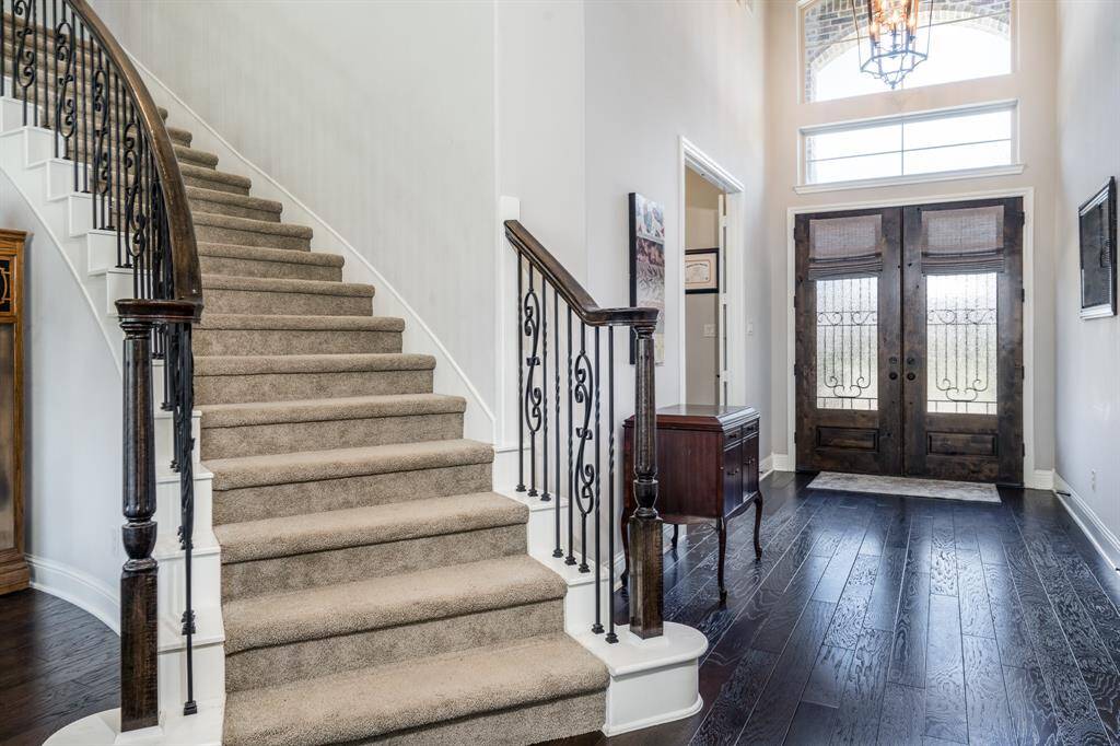 A stylish curved staircase with wrought iron balusters and mahogany double doors with transom windows create the perfect accents to this elegant entry!