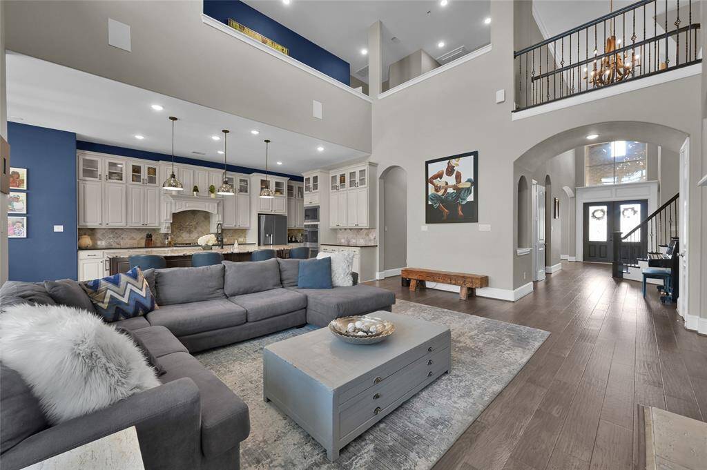 This airy living area features high ceilings and an open floor plan, seamlessly connecting to a modern kitchen with elegant cabinetry and pendant lighting. Rich wooden floors and stylish decor create a welcoming atmosphere, ideal for entertaining or relaxing.