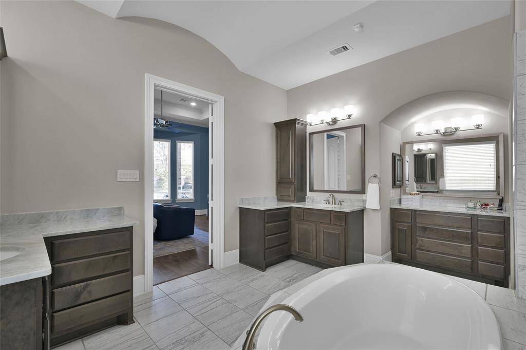 This spacious bathroom features dual vanities with ample storage, elegant lighting, and a freestanding tub. The neutral color scheme and large windows provide a bright, inviting atmosphere.