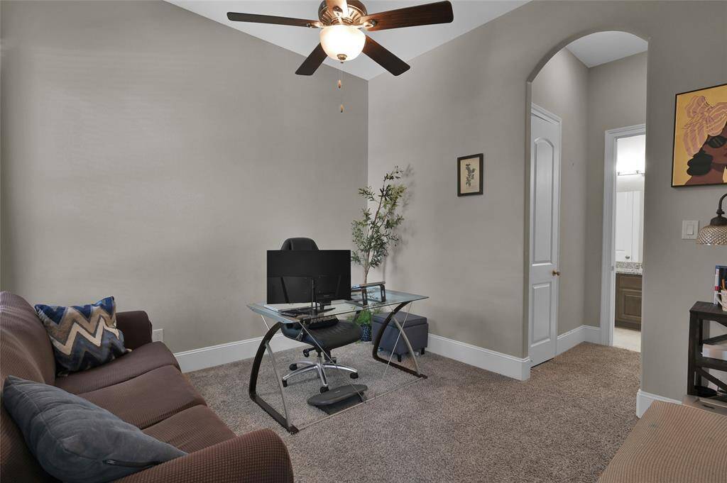 This additional bedroom downstairs is being used as a home office and it  features a ceiling fan, neutral walls, and carpeted flooring.
