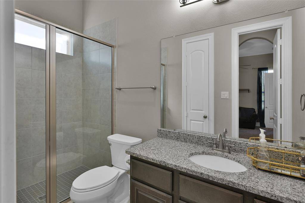 This modern bathroom which features a tiled shower with glass doors, a granite countertop with a single sink, and sleek fixtures is attached to the additional bedroom downstairs.
