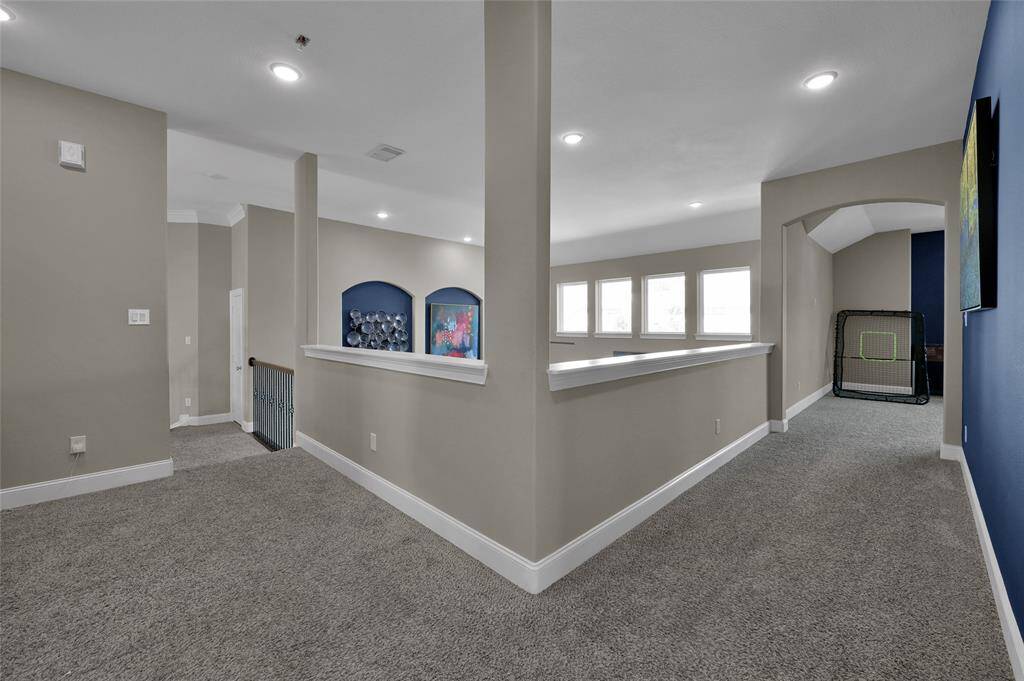 This photo showcases an open, carpeted upstairs area with neutral walls. It includes a hallway with recessed lighting, multiple windows for natural light, and decorative wall niches. There's also a separate alcove, potentially for a game or study area.
