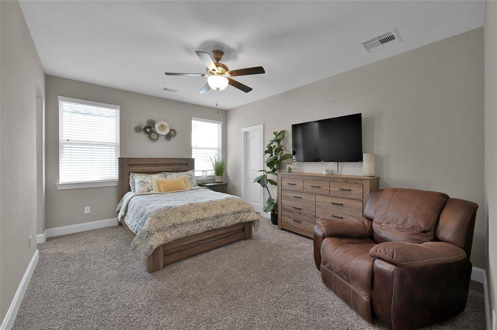 Another photo of this spacious bedroom features neutral walls, plush carpeting, and ample natural light from two windows.