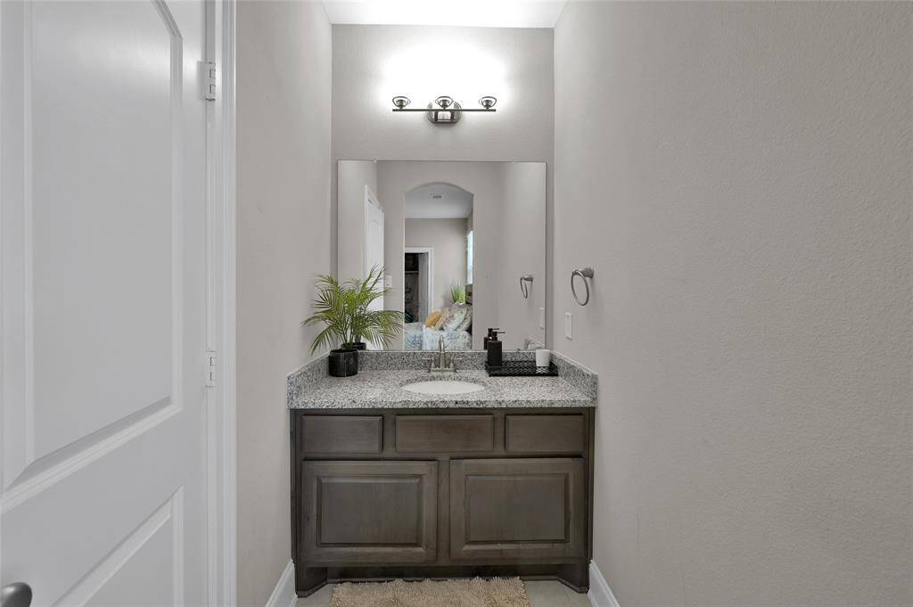 This photo showcases a modern half bathroom next to one of the bedrooms upstairs with a granite countertop vanity, dark wood cabinetry, a large mirror, and contemporary lighting. This bedroom has a jack and jill bath that has an entry door to the hallway for added convience to guests who are in game room or media room.