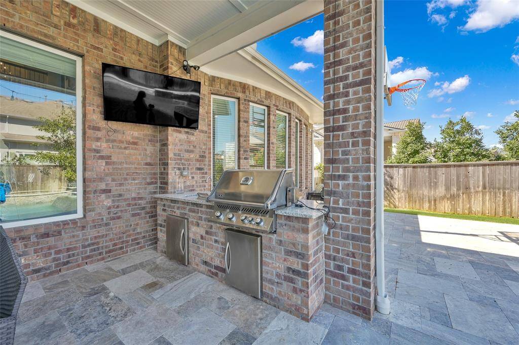 This outdoor space features a covered patio with a built-in grill and countertop, perfect for entertaining. It overlooks a fenced yard with a basketball hoop, providing a great area for relaxation and recreation.