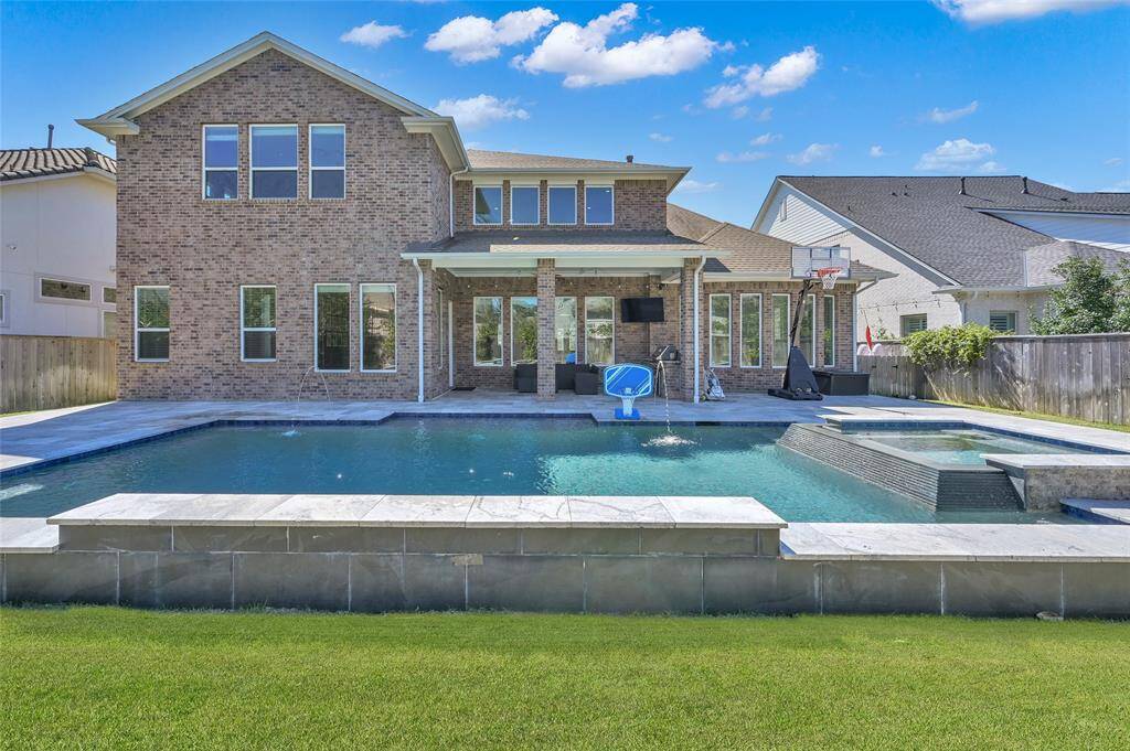 This photo showcases the spacious backyard featuring a large swimming pool, hot tub, and a covered patio area perfect for outdoor entertainment.