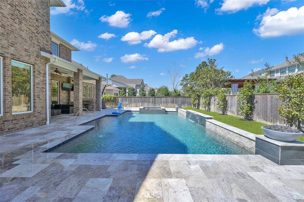 This backyard features a spacious in-ground pool with a stone deck, surrounded by a privacy fence and lush landscaping. The adjacent covered patio provides outdoor living space, perfect for relaxation and entertaining.