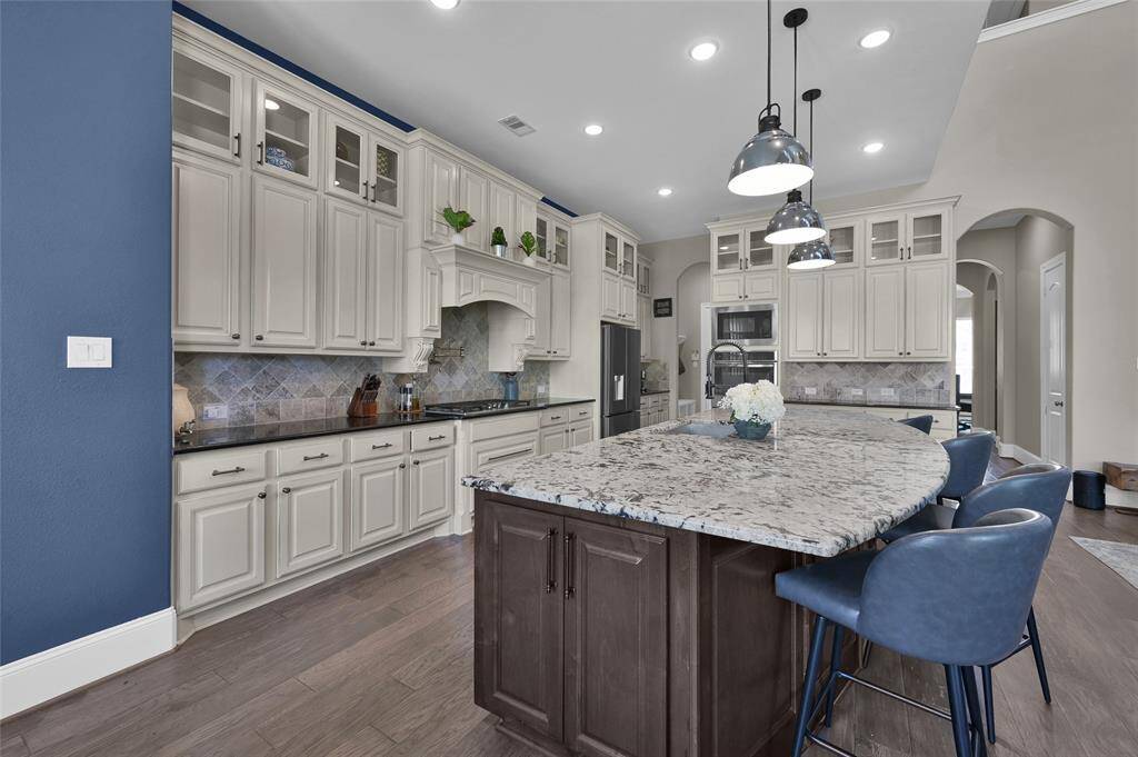 This kitchen features elegant cream cabinetry and a large island with granite countertops. It's accented by modern pendant lighting and blue wall highlights, offering a spacious and stylish cooking area.