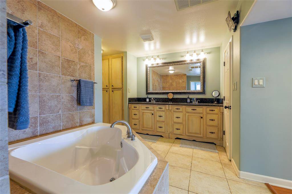 This spacious bathroom features a luxurious soaking tub, double vanity with ample storage, elegant tile work, and a large mirror. Soft lighting and neutral tones create a relaxing atmosphere.