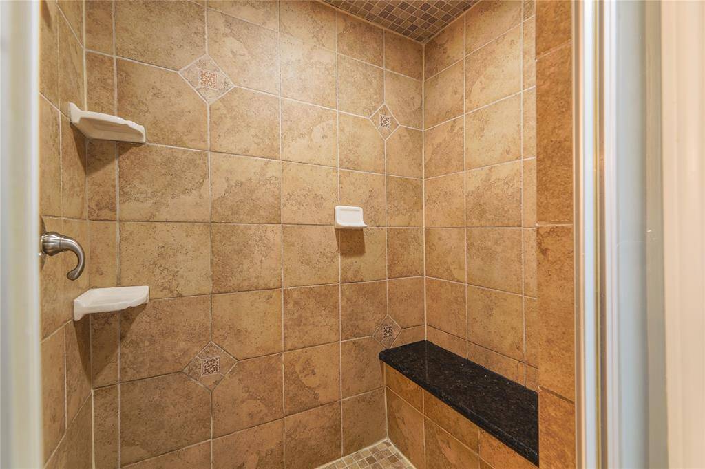 This photo showcases a spacious, tiled walk-in shower with neutral tones, featuring built-in shelves and a bench for convenience and comfort.