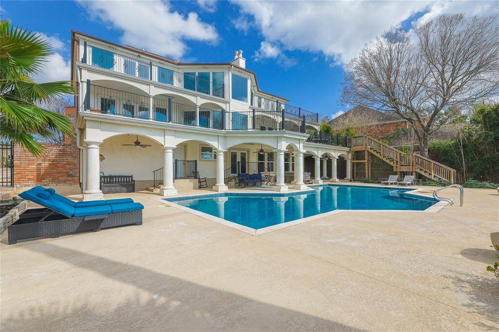 This photo showcases a luxurious outdoor space featuring a covered patio with elegant columns, a swimming pool, and a hot tub. The area overlooks a serene waterfront with a thatched-roof structure, creating a perfect setting for relaxation and entertaining.