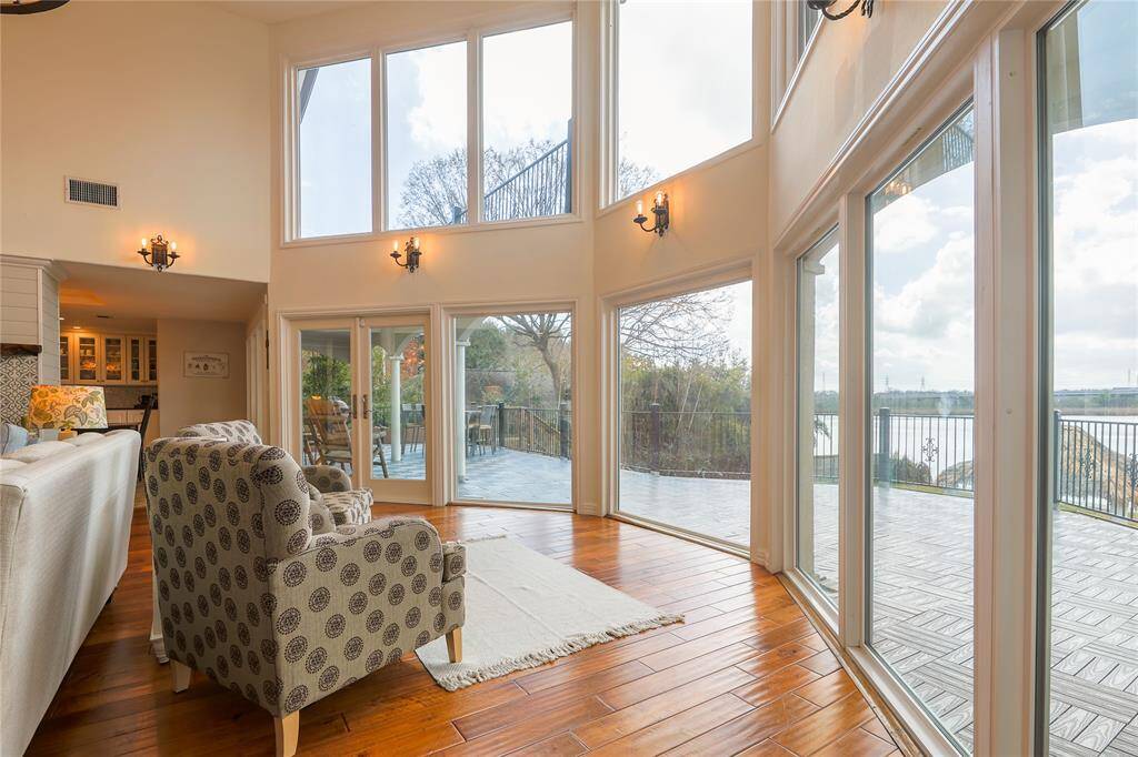 This bright living area features expansive floor-to-ceiling windows offering stunning views and abundant natural light. The warm hardwood floors and cozy seating create an inviting atmosphere, complemented by access to a spacious outdoor deck.