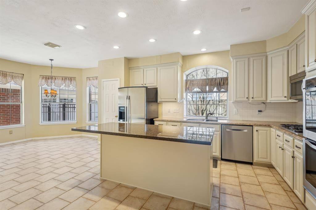 This spacious kitchen features sleek granite countertops, stainless steel appliances, and ample cabinetry. It offers a bright breakfast area with large windows and a tiled floor, perfect for family dining.