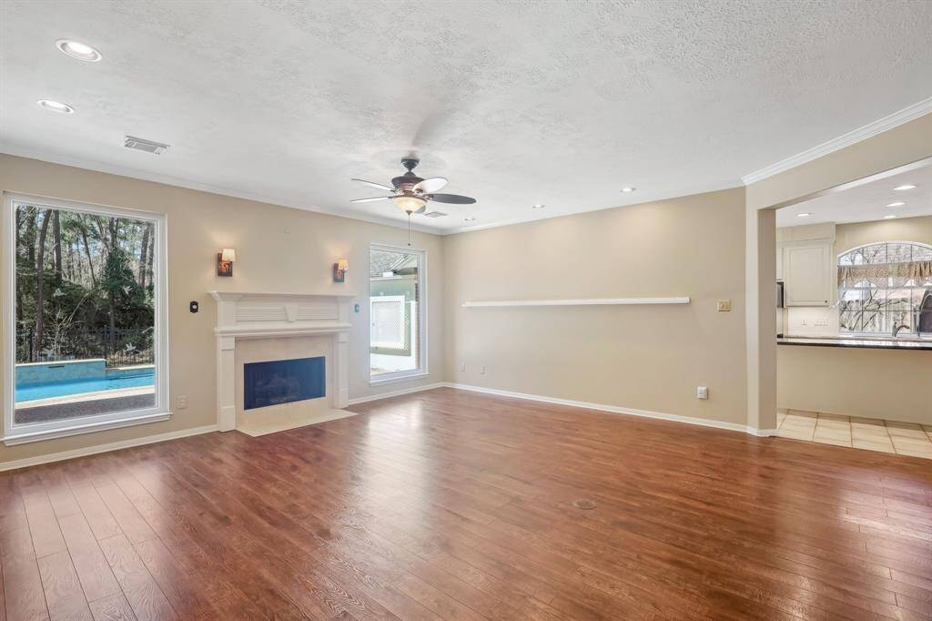 This spacious living room features hardwood floors, a cozy fireplace, and large windows offering plenty of natural light with a view of the pool. It opens to a bright, modern kitchen, creating a seamless flow for entertaining.