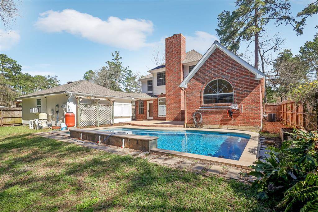 This photo shows a charming brick home with a spacious backyard featuring a pool. The house has a large arched window and a chimney, surrounded by trees and a wooden fence, offering a private and inviting outdoor space.