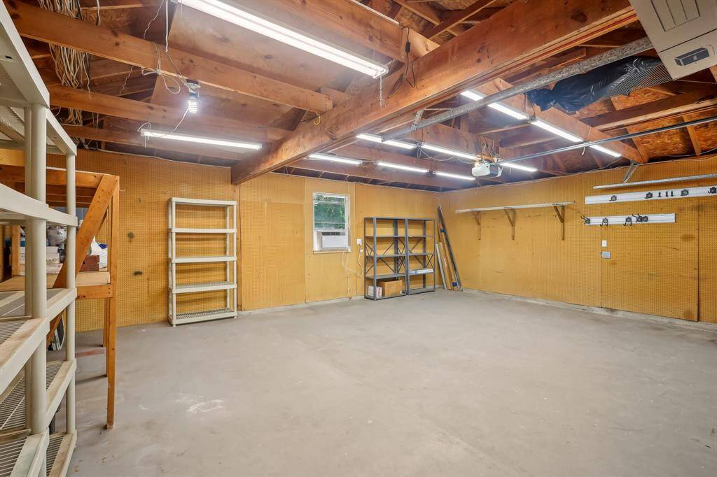 Spacious, well-lit garage with ample shelving and storage options—ideal for organizing tools and projects. Note there is extra width in this garage for bikes, tools, etc