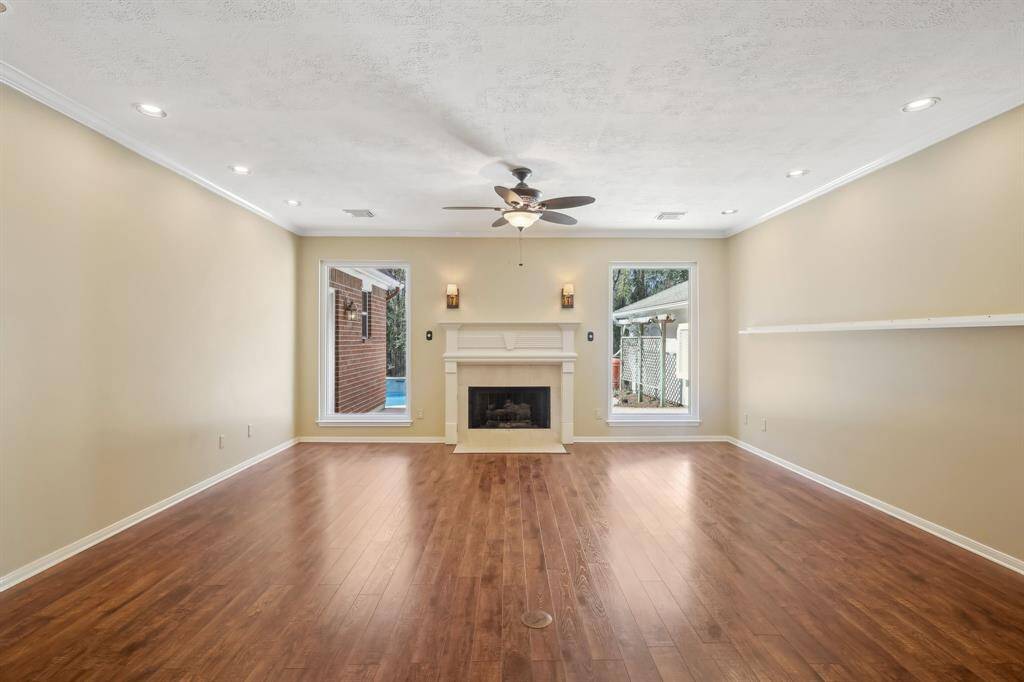 This spacious living room features hardwood floors, a cozy fireplace, recessed lighting, and large windows with views of the outdoors. A ceiling fan adds comfort and style.