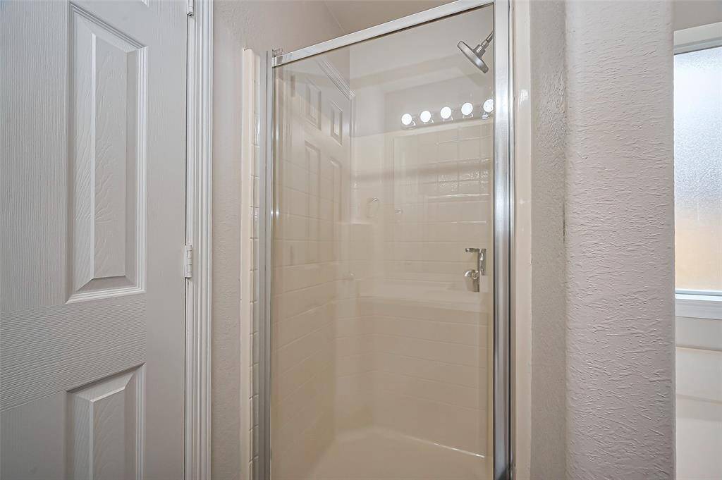 The ensuite bath features a walk-in shower with cultured marble walls and a sleek glass shower door. A door on the left leads to the spacious walk-in closet, providing ample storage and organization. The home also includes a water softener system, which helps reduce mineral buildup in pipes and appliances, extends the lifespan of plumbing fixtures, and provides softer water for bathing, cleaning, and laundry.