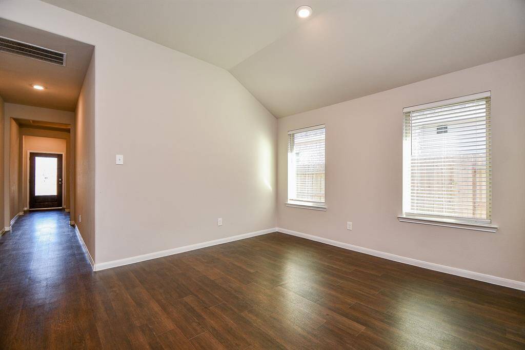 This photo shows a bright and airy room with high ceilings and hardwood floors. It features two large windows letting in natural light. A hallway leads to a door, adding depth and flow to the space.