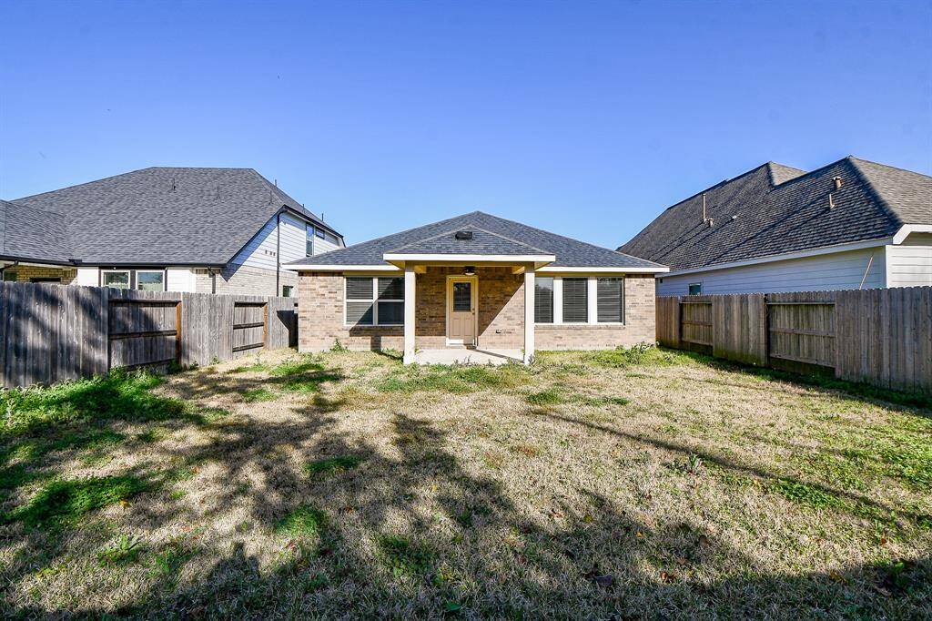 This photo shows a backyard of a single-story brick home featuring a covered patio area. The yard is enclosed by a wooden fence and offers ample grassy space, ideal for outdoor activities or gardening.